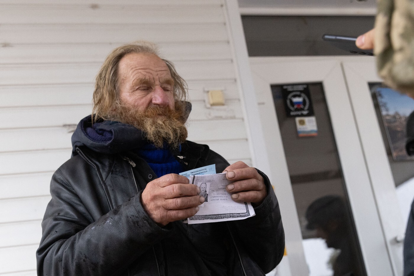 Беженец из Суджанского района Курской области показывает документы военному перед входом в пункт приёма беженцев